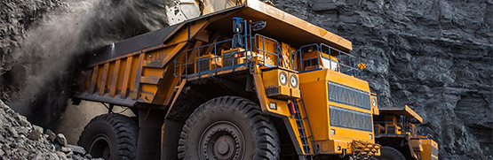Two trucks by a mine wall, one being filled up with material.