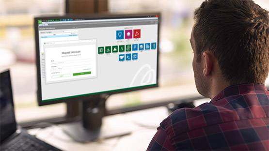 Someone sitting at a desk, looking at a monitor which shows the Maptek Account interface.